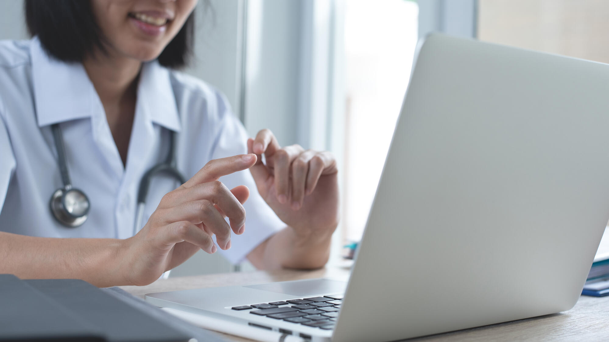 Female doctor video calling, using zoom meeting online app via laptop computer in medical office, close up