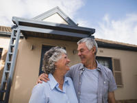 An elder couple standing outside of their home, smiling at one another